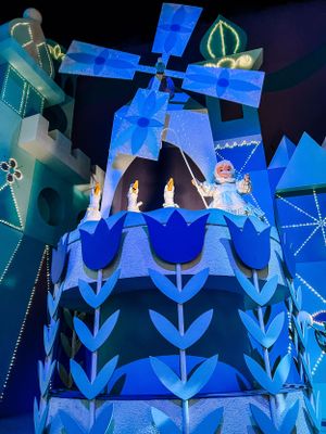 A blue and white castle facade with windmill style decorations lit up at night during Disney's It's a Small World attraction.