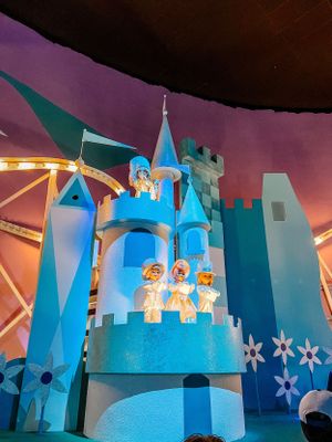 A blue illuminated castle with turrets and white snowflakes at Disney's It's a Small World attraction during nighttime.