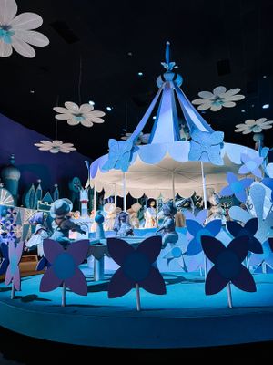 A carousel-style display with white daisies and blue butterflies illuminated in cool lighting against a dark background.