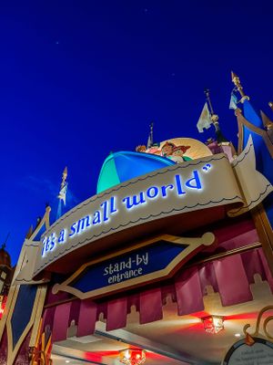 "it's a small world" attraction entrance sign illuminated at night against a deep blue sky at Disney theme park.
