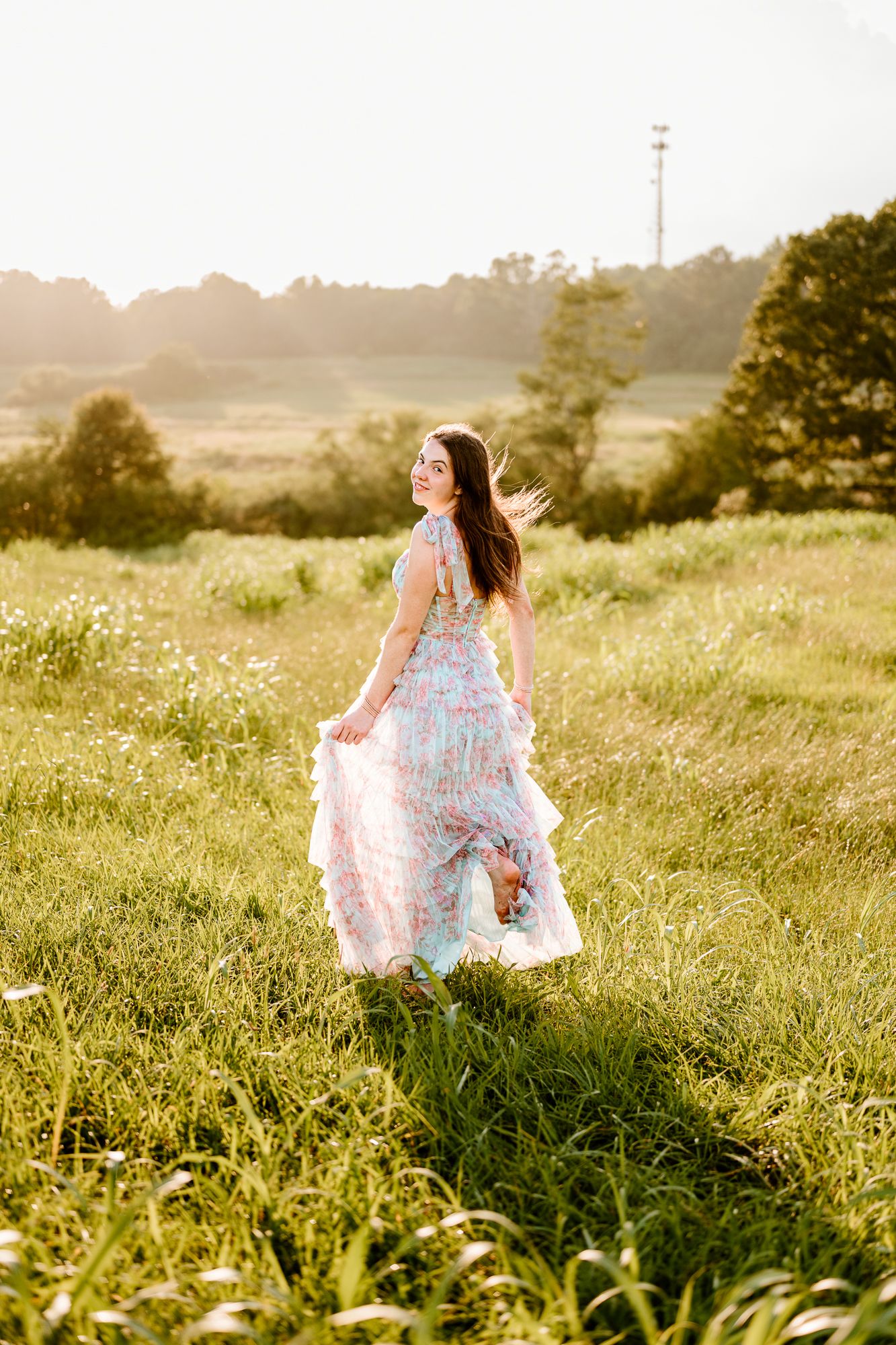 A figure in a flowing floral dress twirls through a sunlit meadow at golden hour, creating a dreamy summer scene.