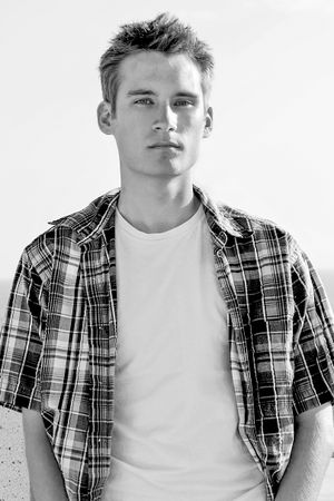 Black and white portrait in plaid short-sleeve shirt against light background.