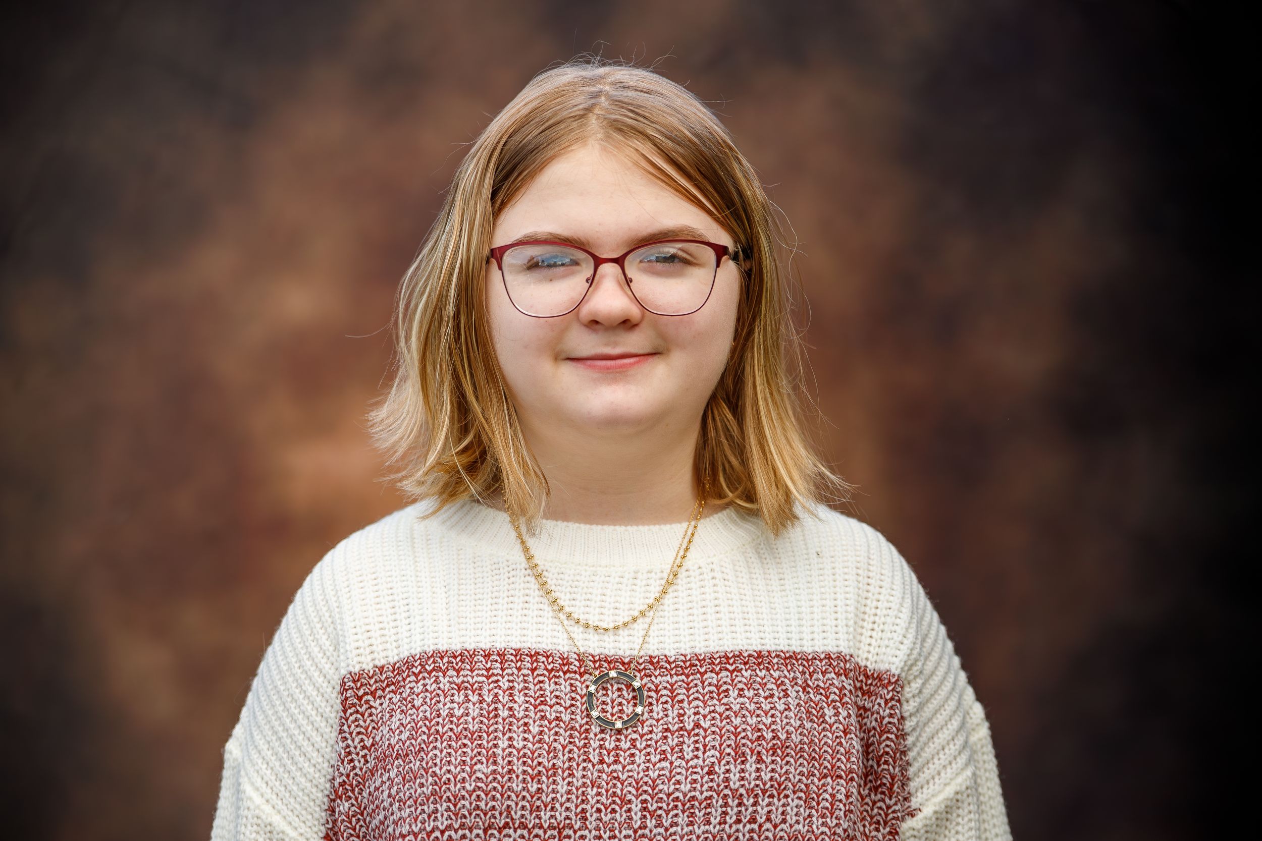 Portrait showing glasses and a white and pink sweater against a brown backdrop.