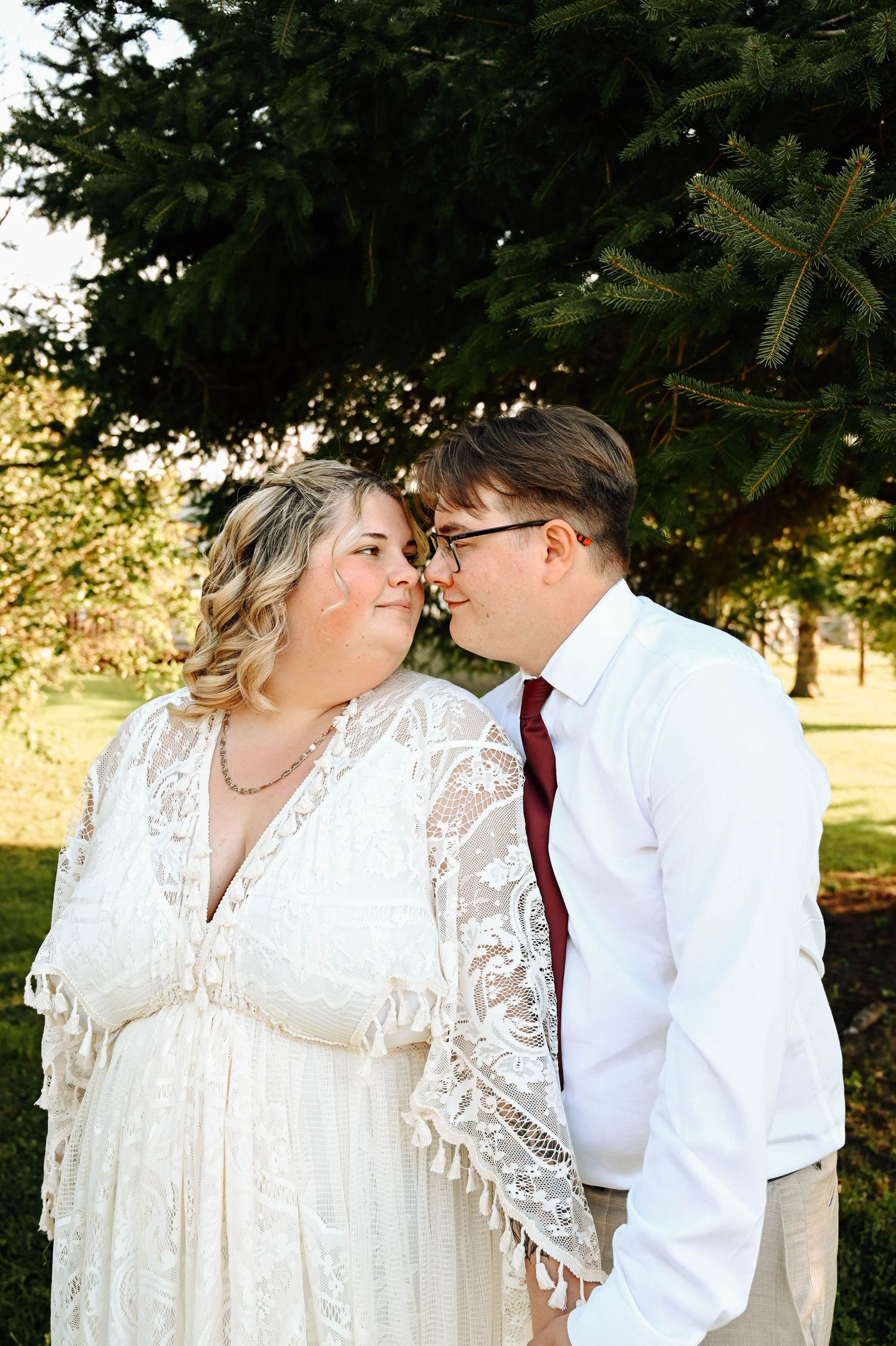 An outdoor wedding ceremony with wooden church pews set up on grass under sunny skies surrounded by trees.