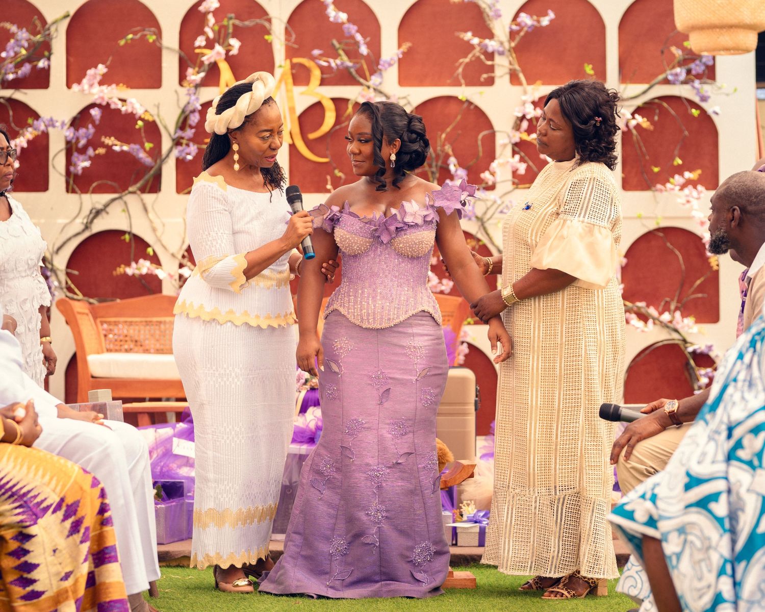 Group celebrates at outdoor event wearing elegant purple and cream traditional attire.