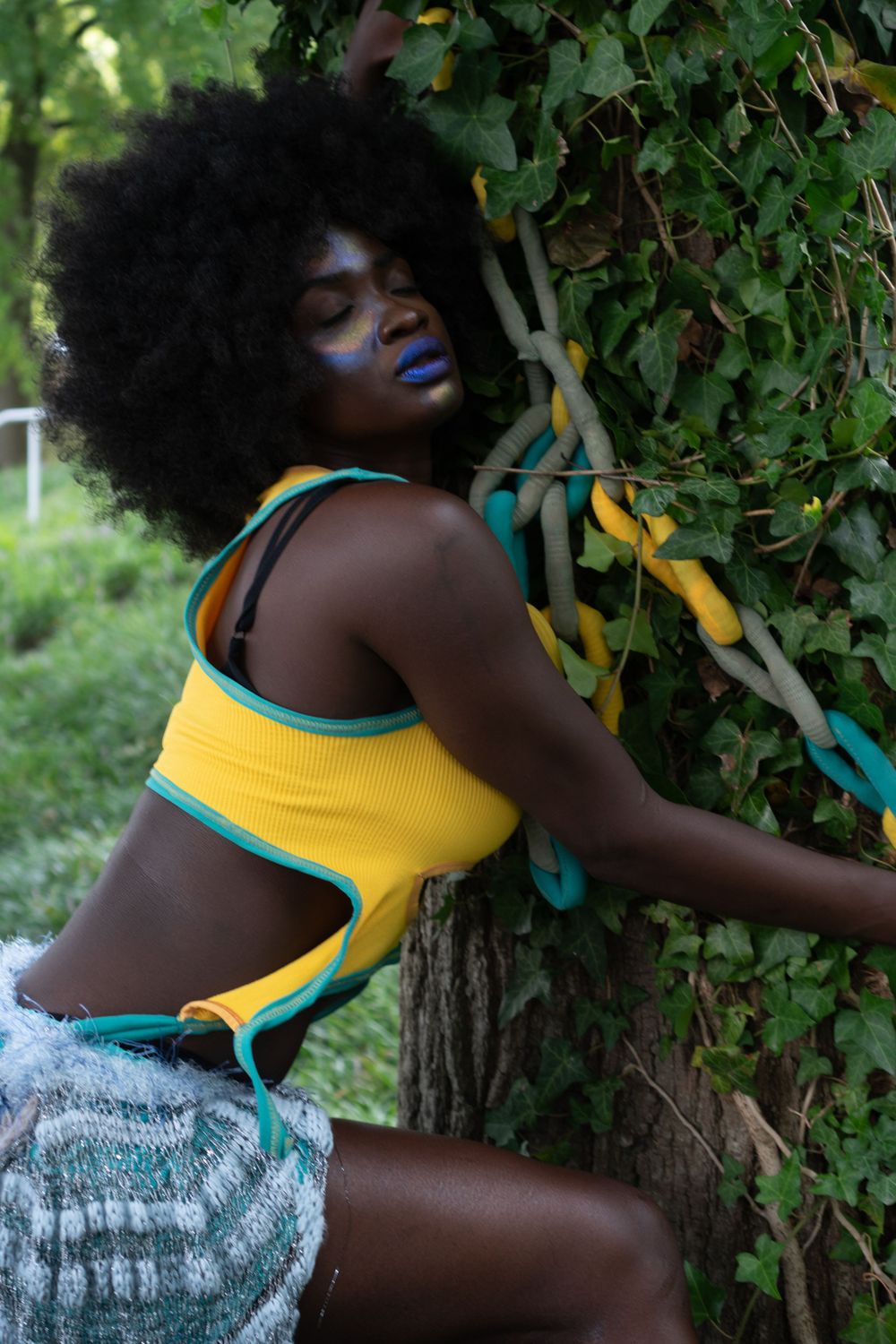 Summer fashion portrait with yellow tank top grabbing onto a tree with felt ‘chains’ in a tree hugger style.