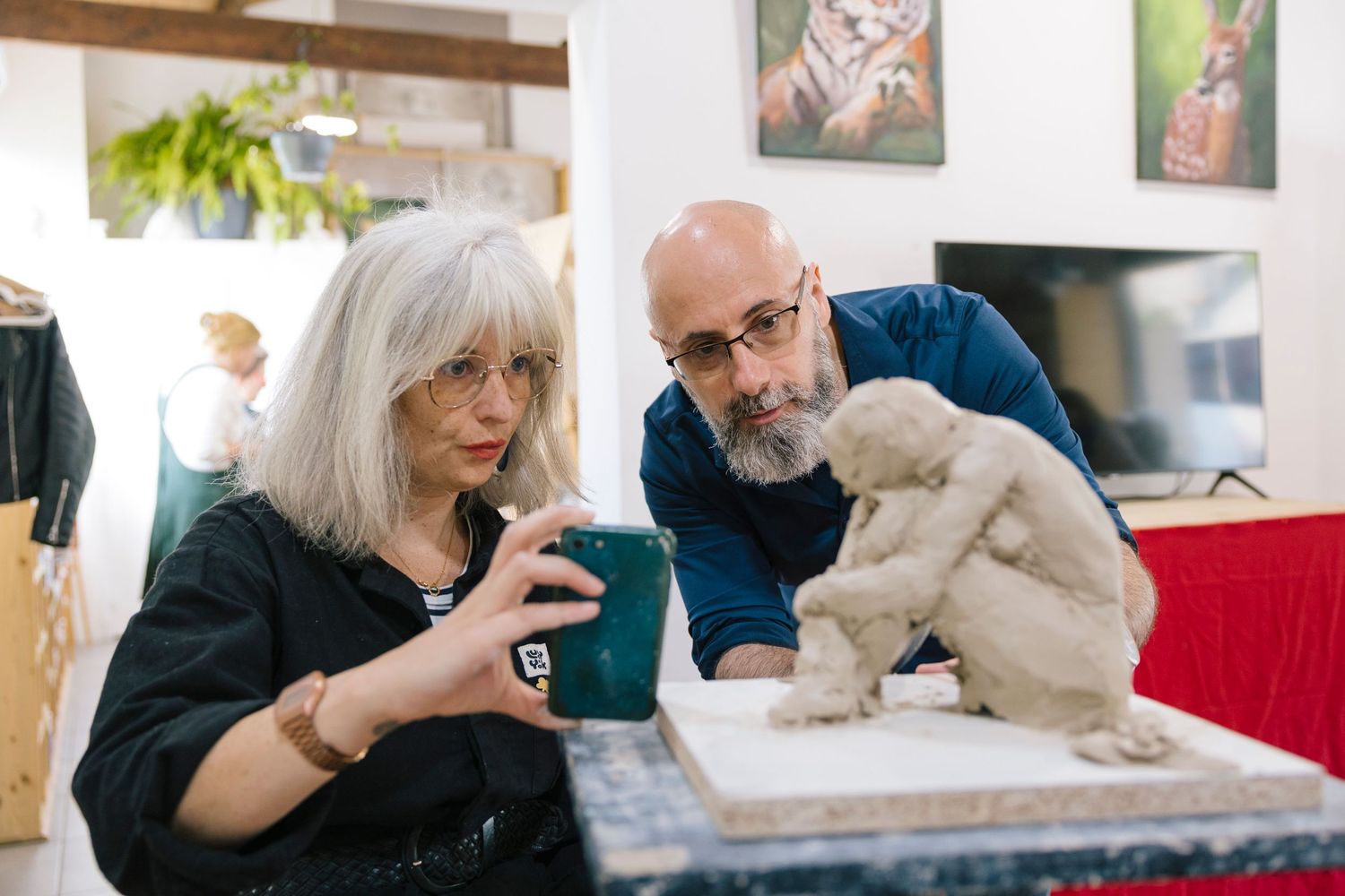 Two people examining a small sculpture on a table with artwork displayed on walls.