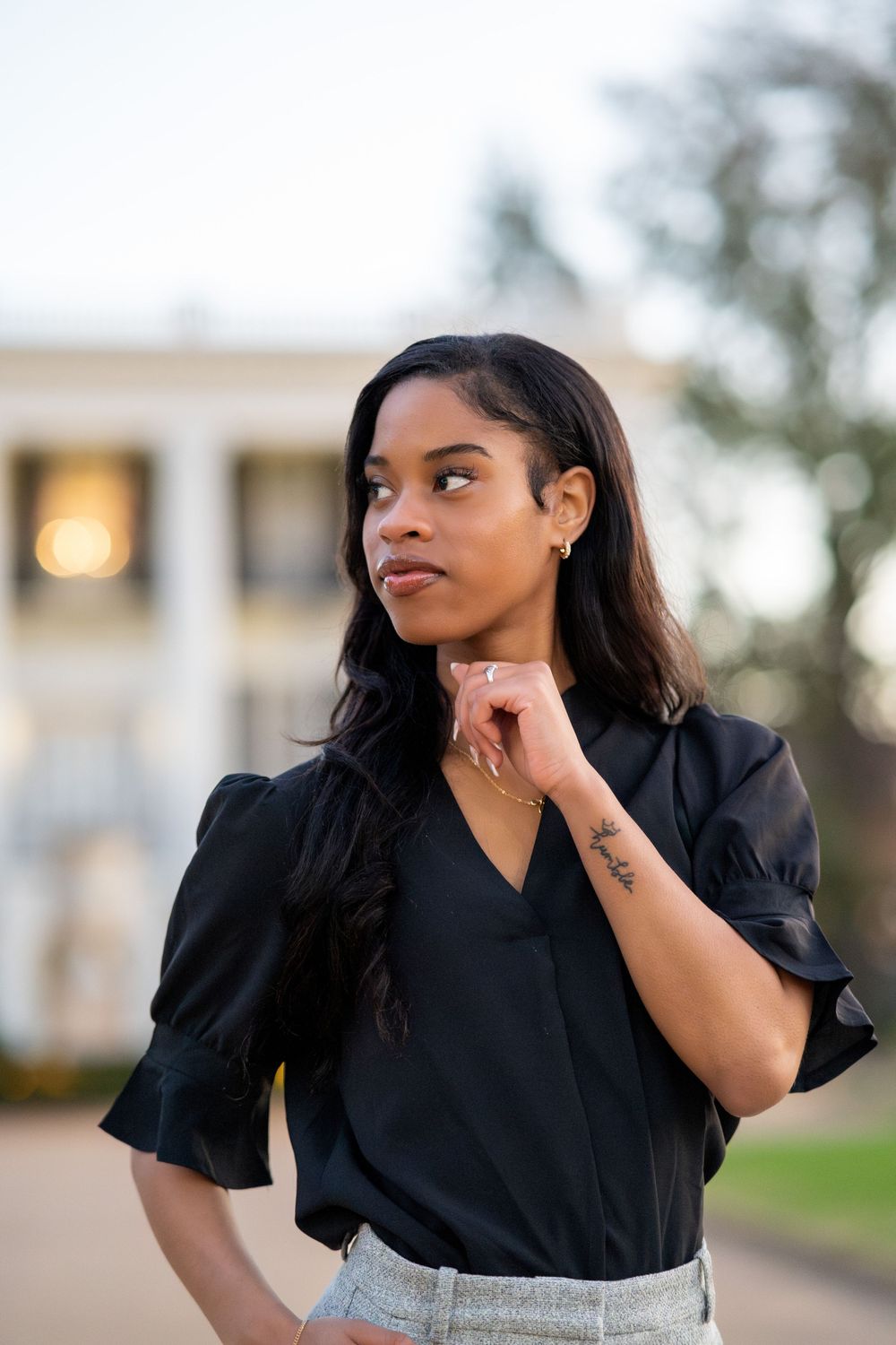 Portrait of someone in a black blouse and hoop earrings thoughtfully looking to the side outside a building at sunset.