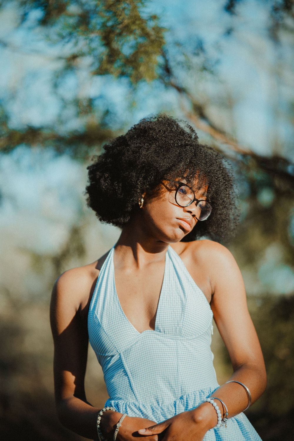 Beautiful portrait of someone wearing glasses and a light blue halter dress posing outdoors in natural sunlight.