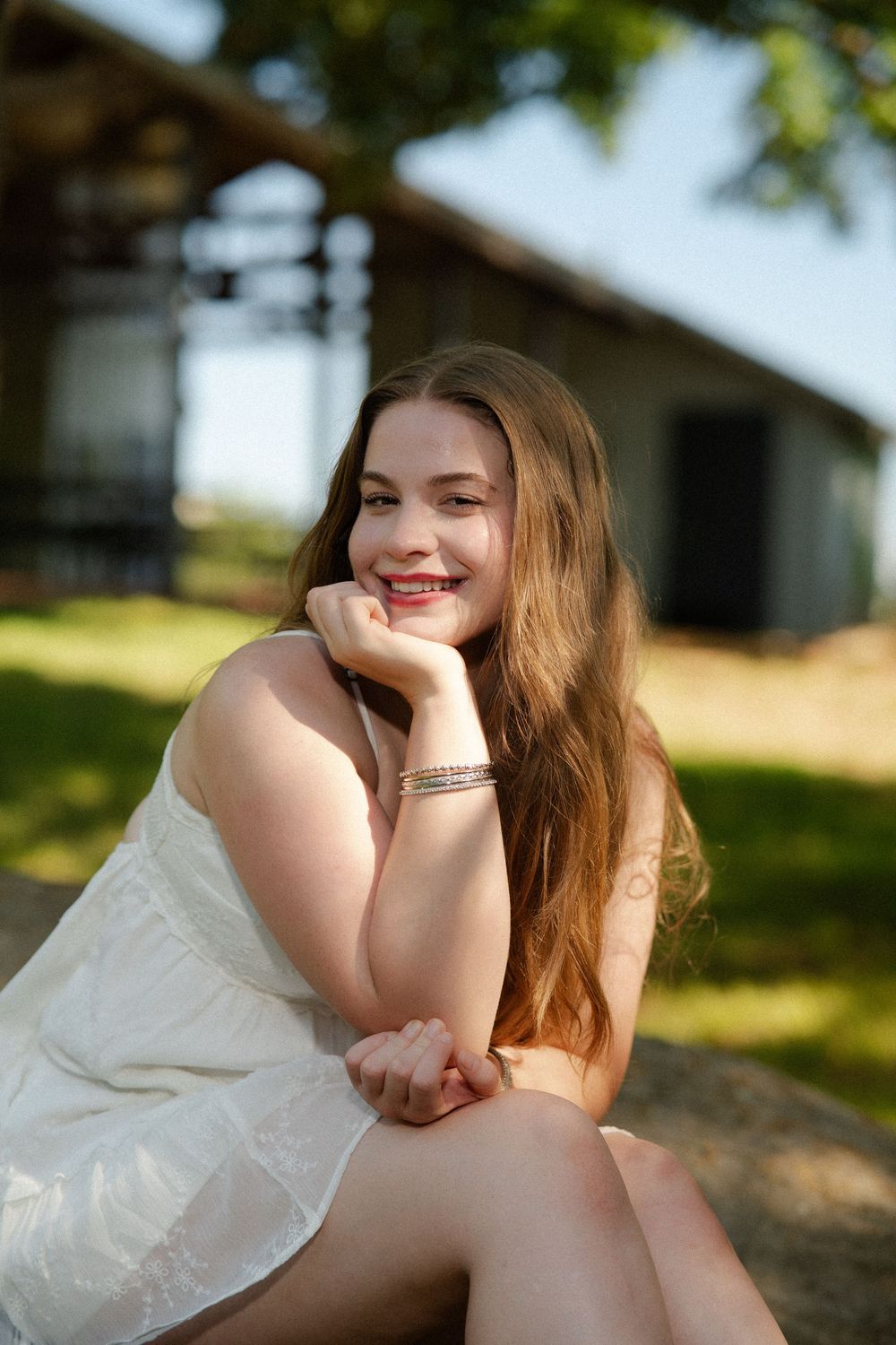 Outdoor portrait series showing a person in a flowing white dress sitting on the ground in warm natural sunlight.