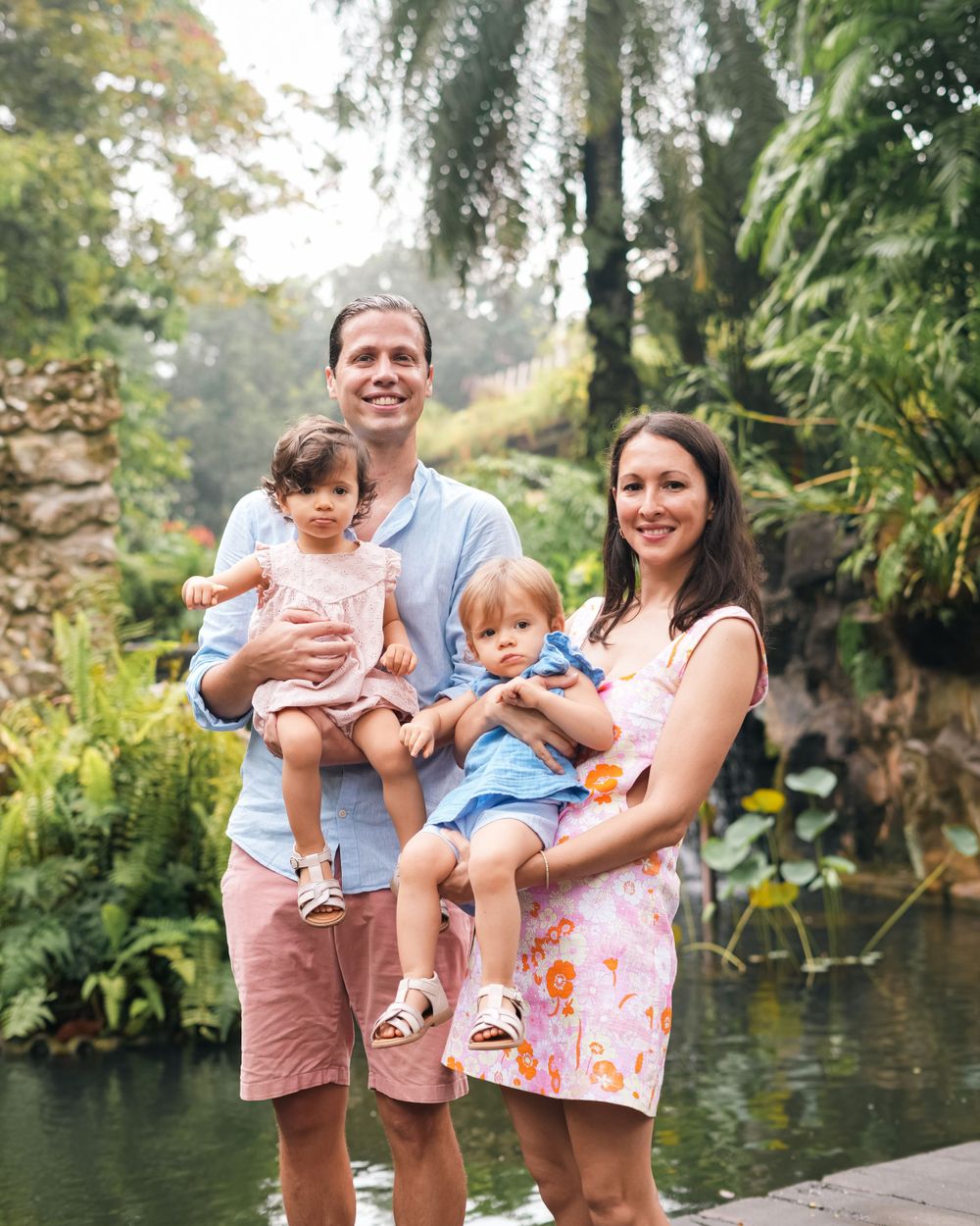 A family poses together near a pond surrounded by tropical plants.