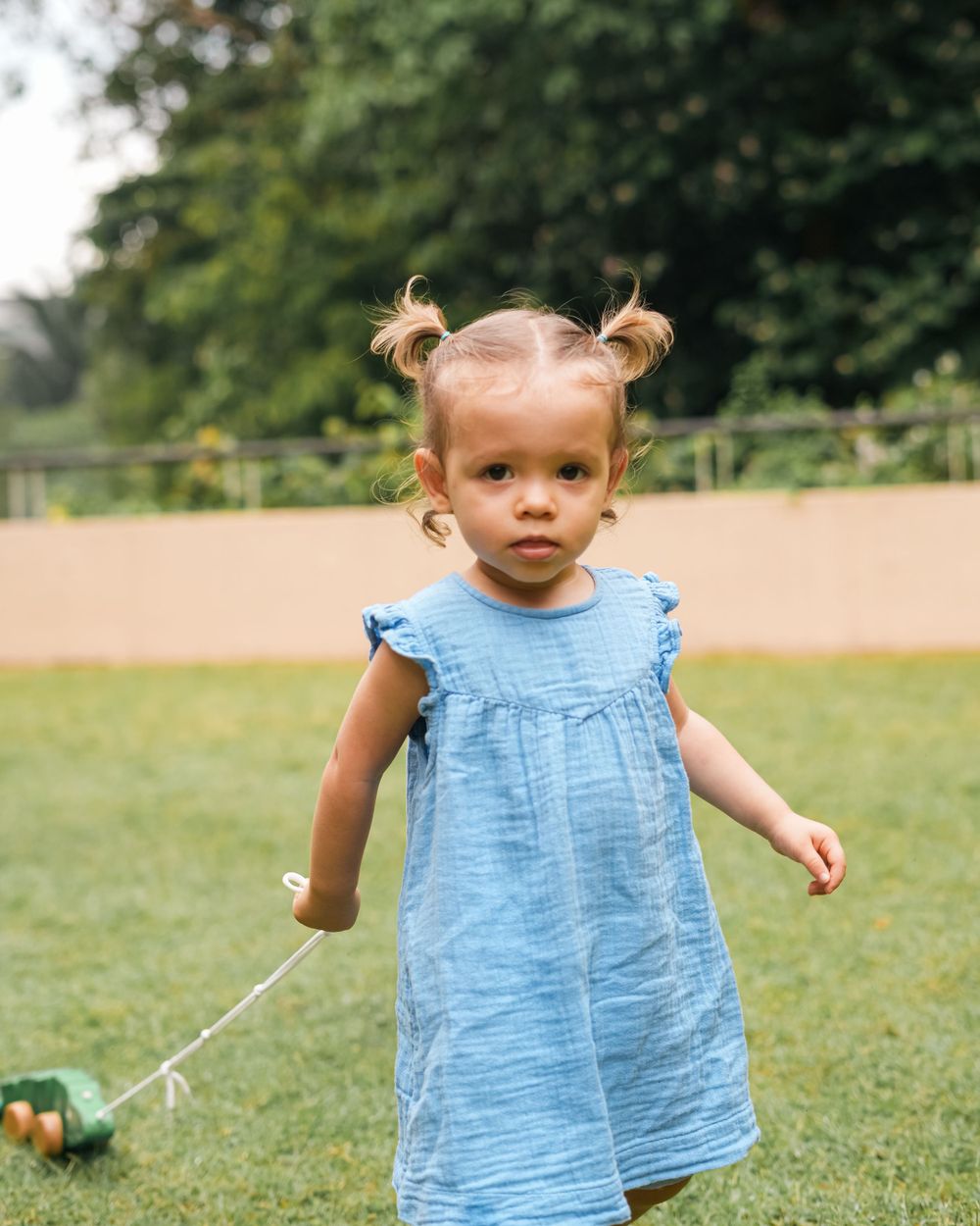 A toddler in a blue dress plays in a sunny garden.