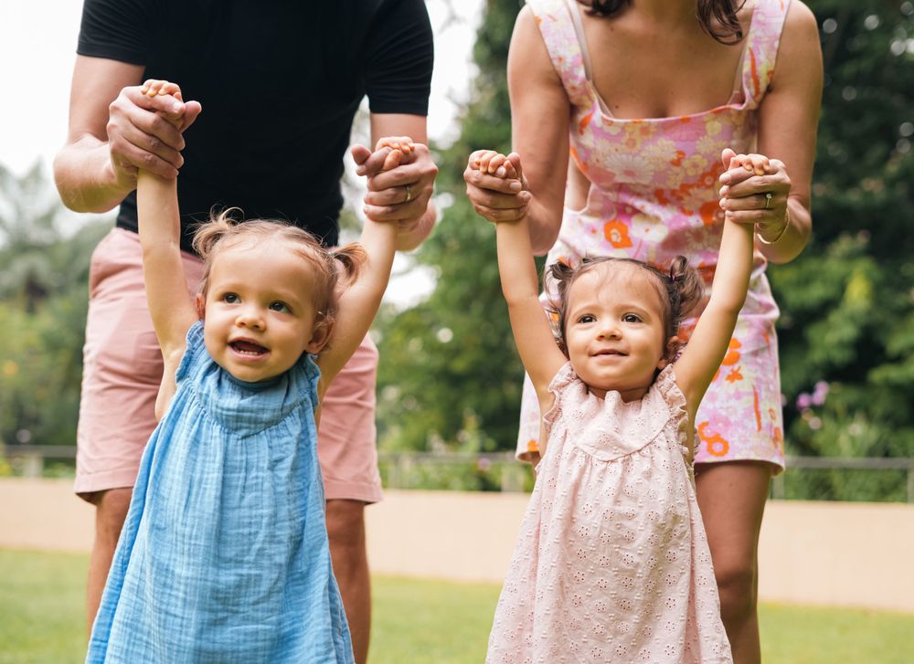 Parents hold hands with their children while playing outdoors.