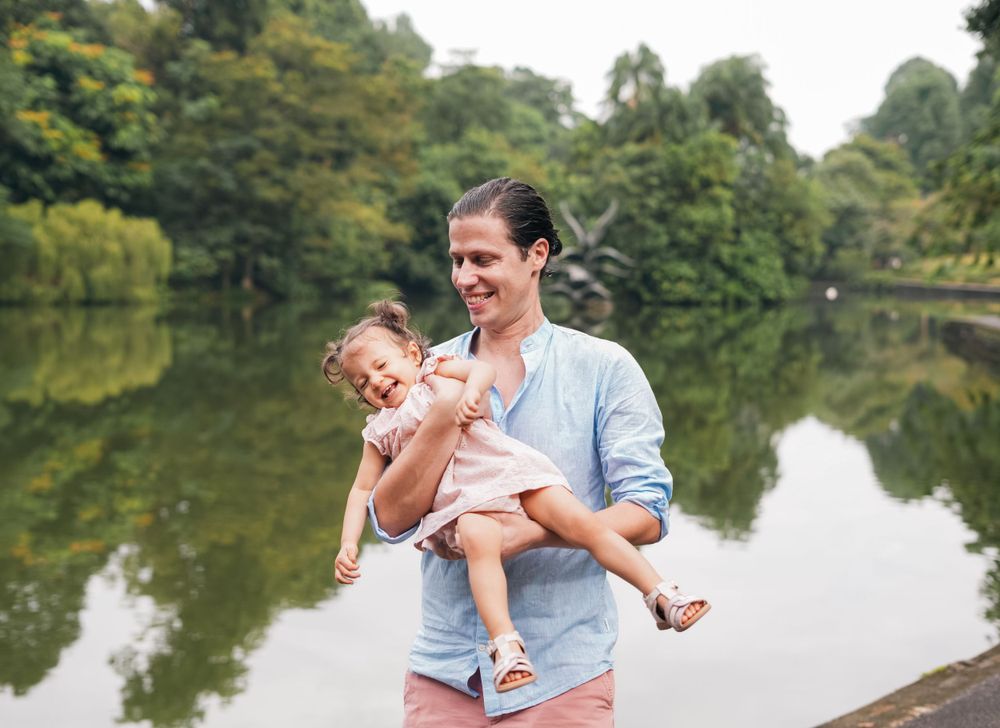 A tender moment captured by a serene pond with lush greenery in the background.