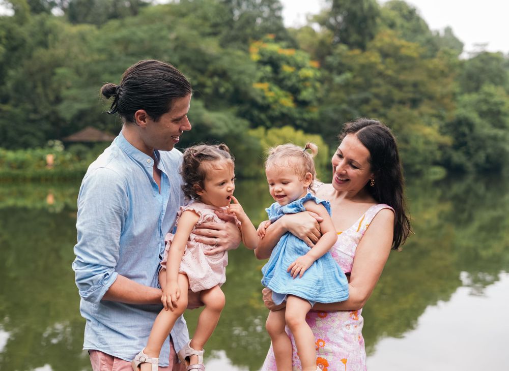 A family portrait taken outdoors with a scenic lake and trees in the background.