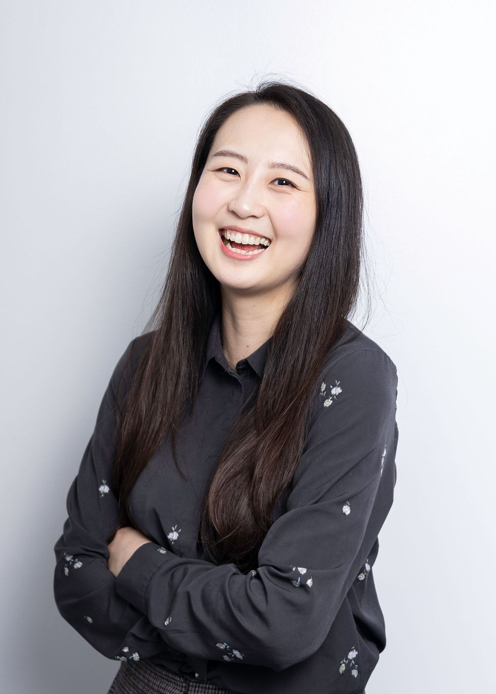 Professional headshot of person in dark floral print shirt against light background.