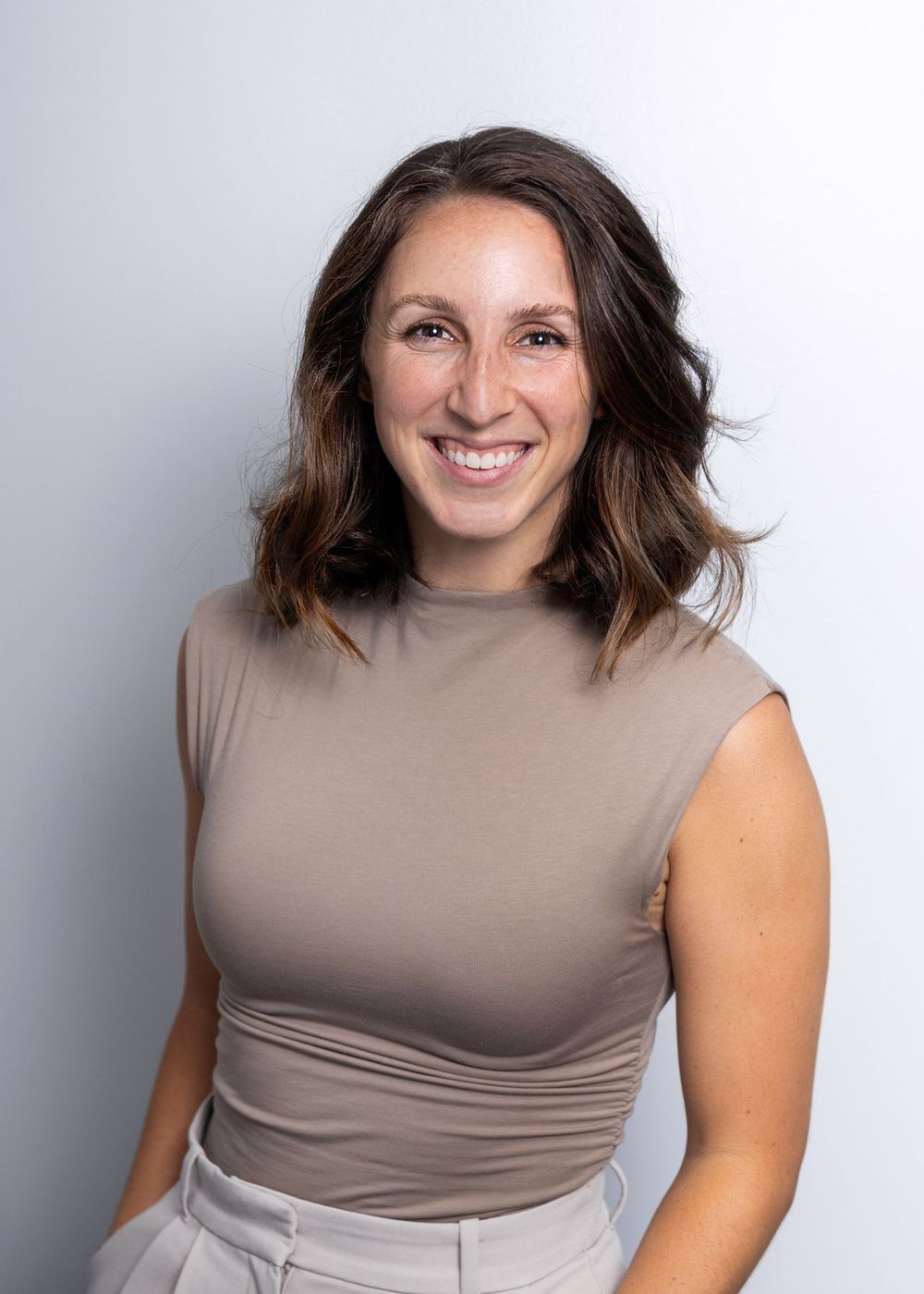 Professional headshot of a person wearing a beige sleeveless turtleneck against a light gray background.