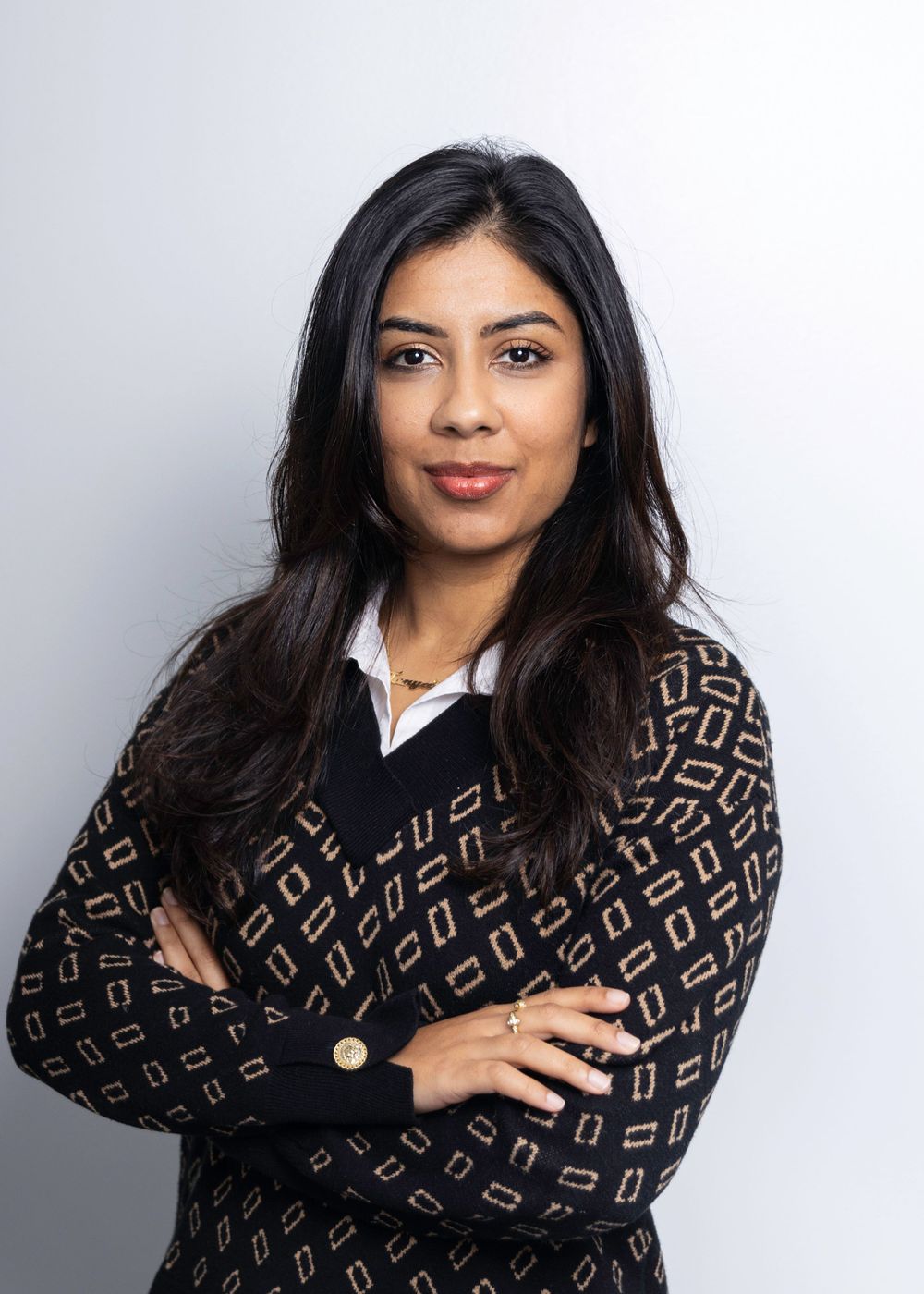 Professional studio portrait of someone with long dark hair wearing a patterned black sweater against a light gray background.