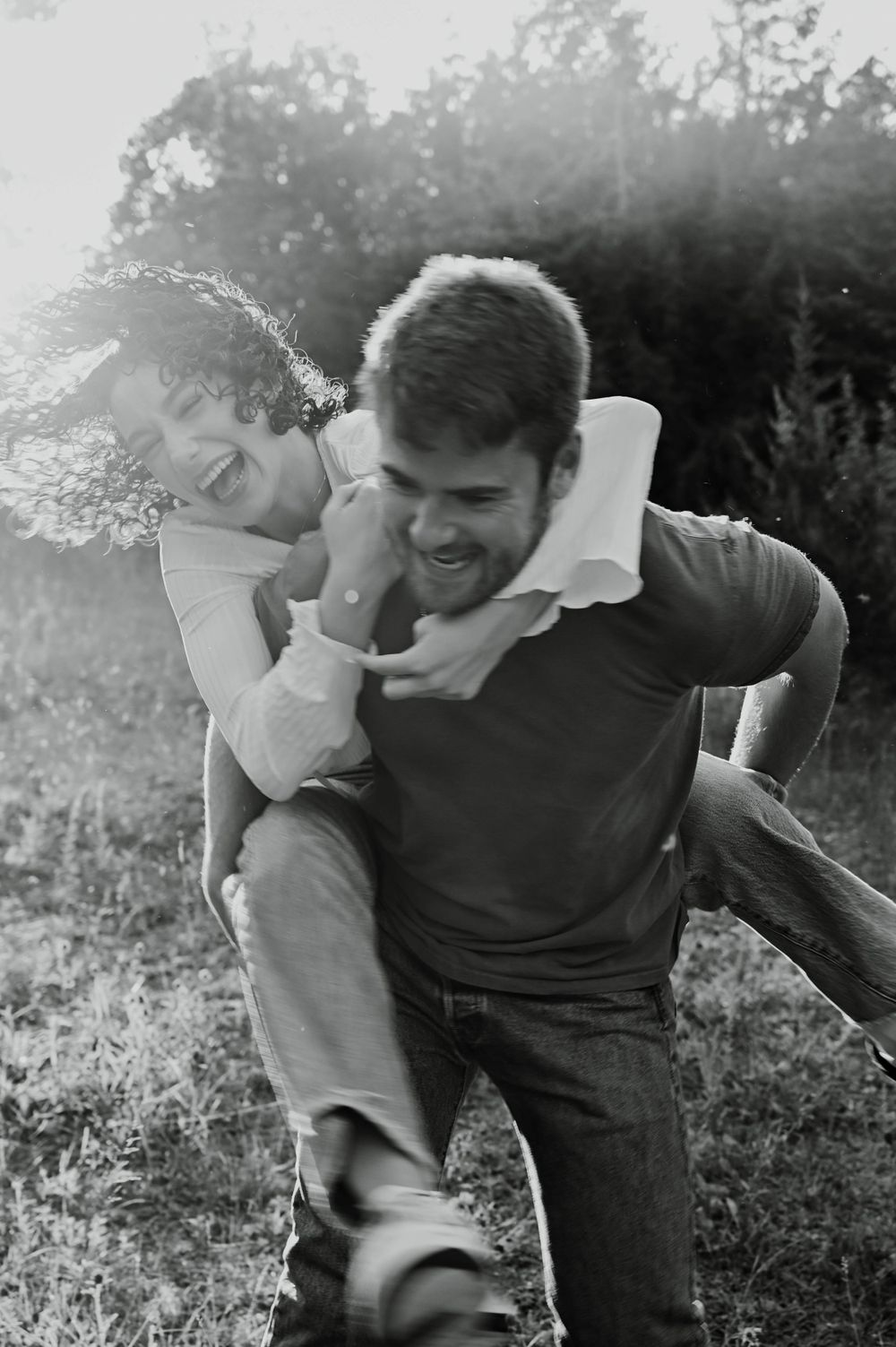 A playful black and white moment captured outdoors with sunlight streaming through trees in the background.