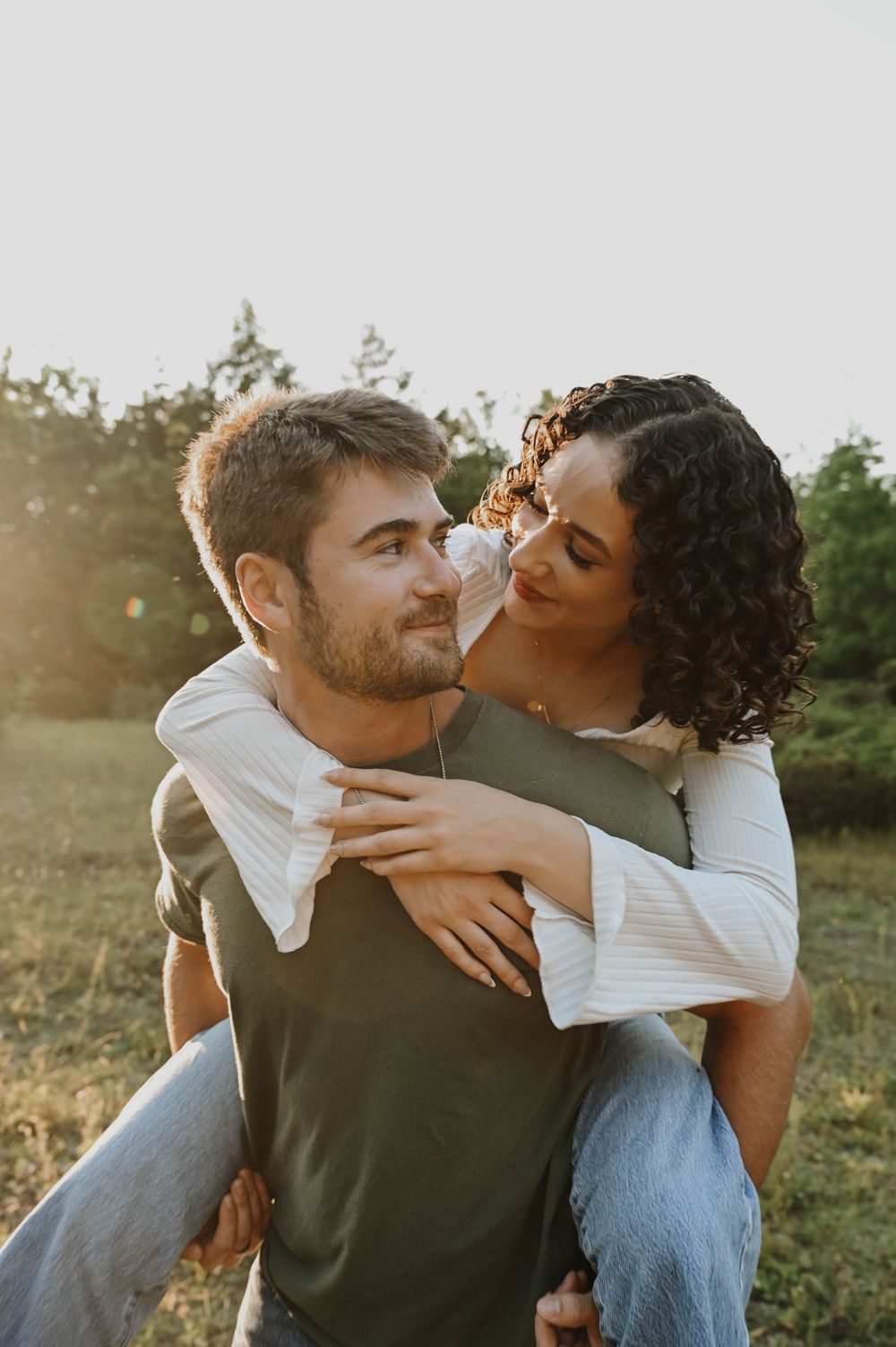 A romantic piggyback moment between a couple outdoors during golden hour in a grassy field.
