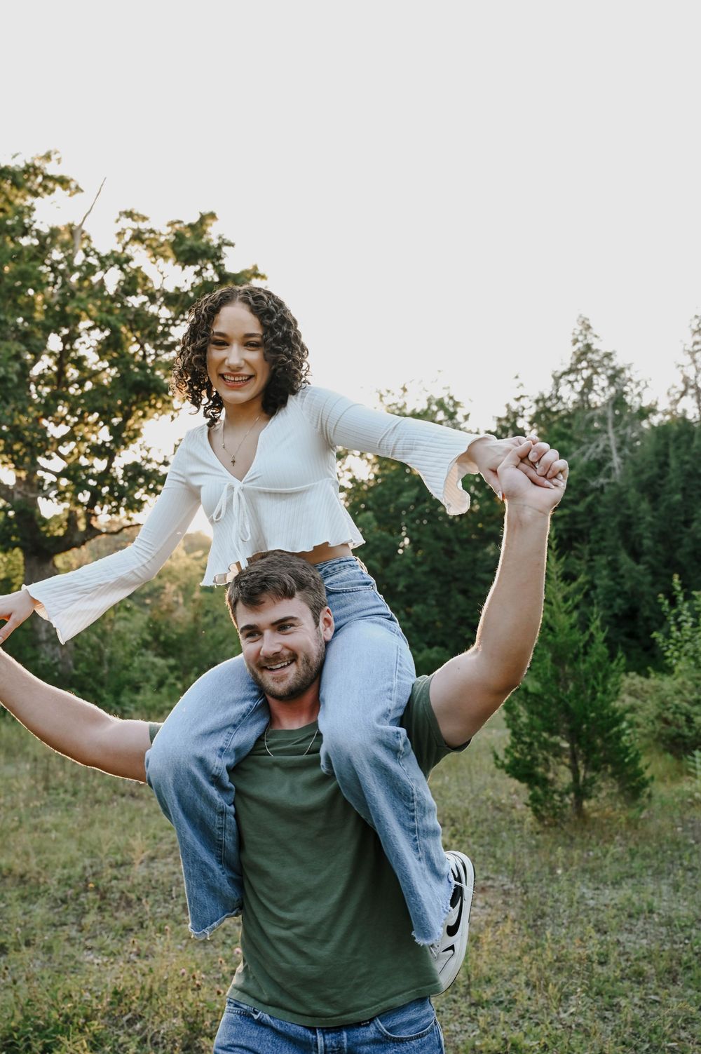 A playful couple enjoying a piggyback ride outdoors in a natural setting with trees and greenery in the background.