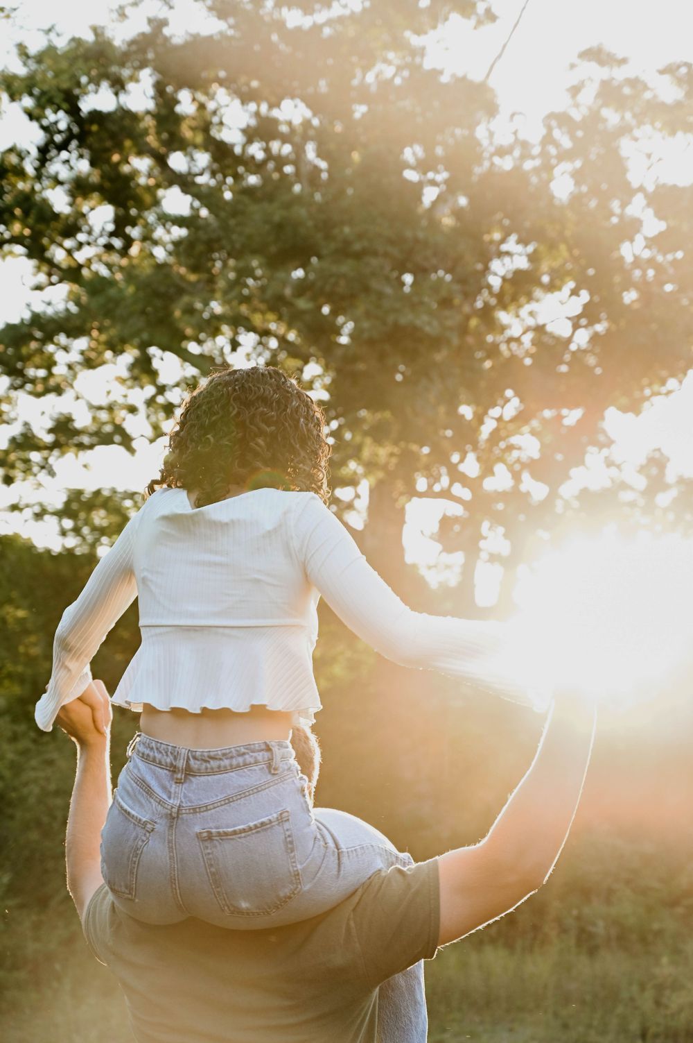 A couple embraces in a romantic moment against golden sunlight filtering through trees during sunset.