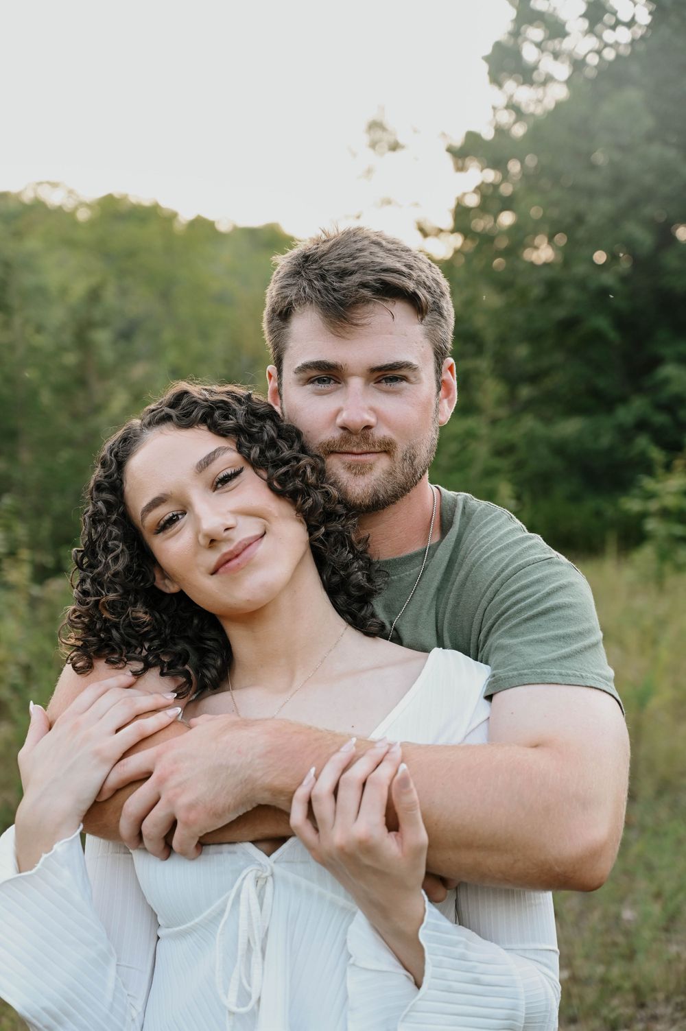A romantic outdoor portrait of a couple embracing in a natural setting during golden hour.
