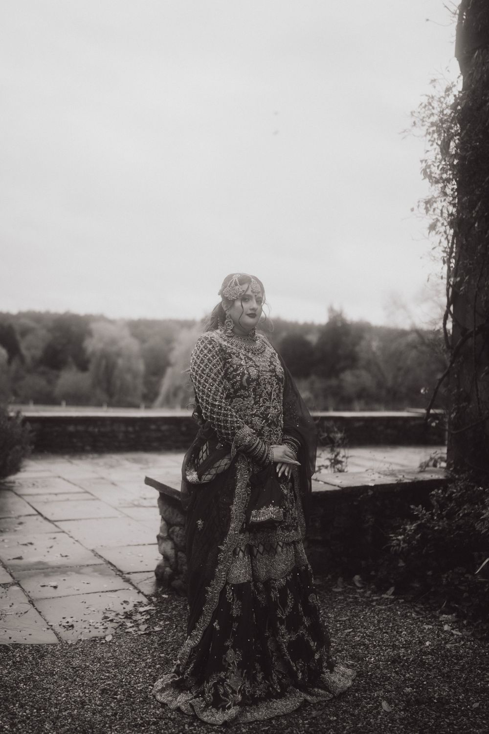 Atmospheric black and white portrait of a person in vintage dress on a stone terrace.