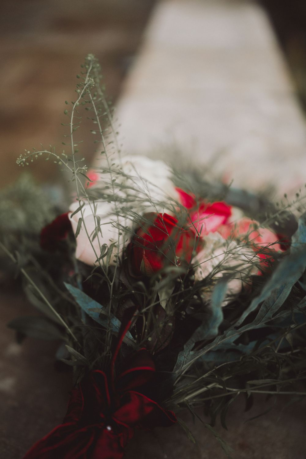 Moody floral arrangement with red blooms and delicate greenery against blurred background.