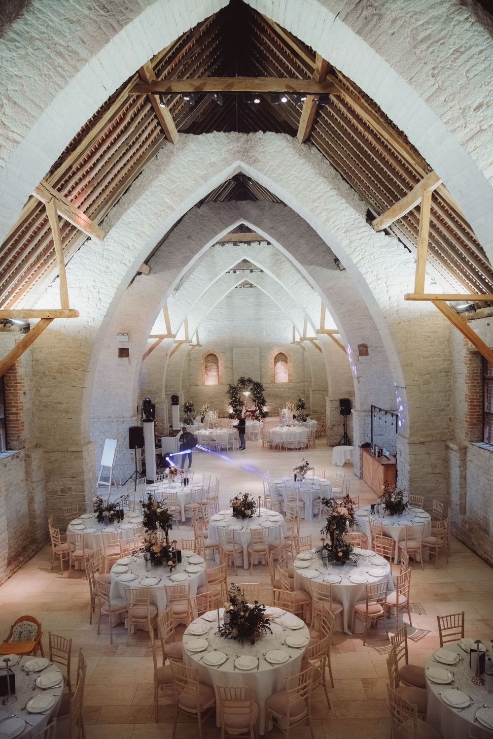 Elegant wedding reception setup in a vaulted white stone chapel with round tables and exposed beams.