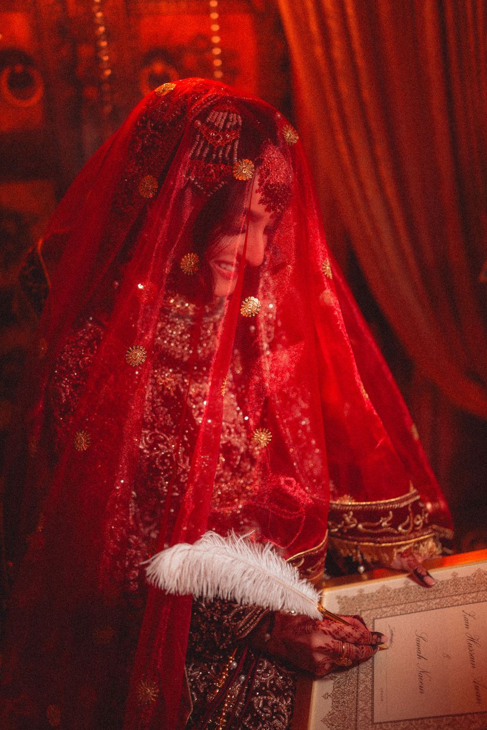 South Asian bride in red veil and traditional attire against red drapery background.
