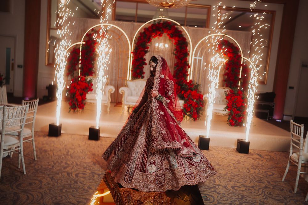 Ornate wedding attire twirling under illuminated arches decorated with red flowers and fairy lights.