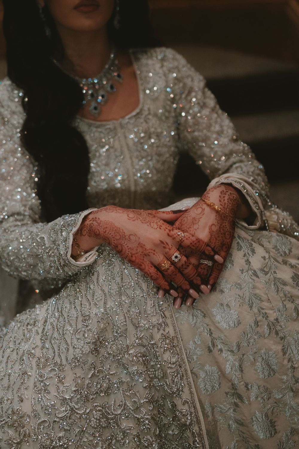 Close-up of intricate henna designs on hands against a sparkly white dress.