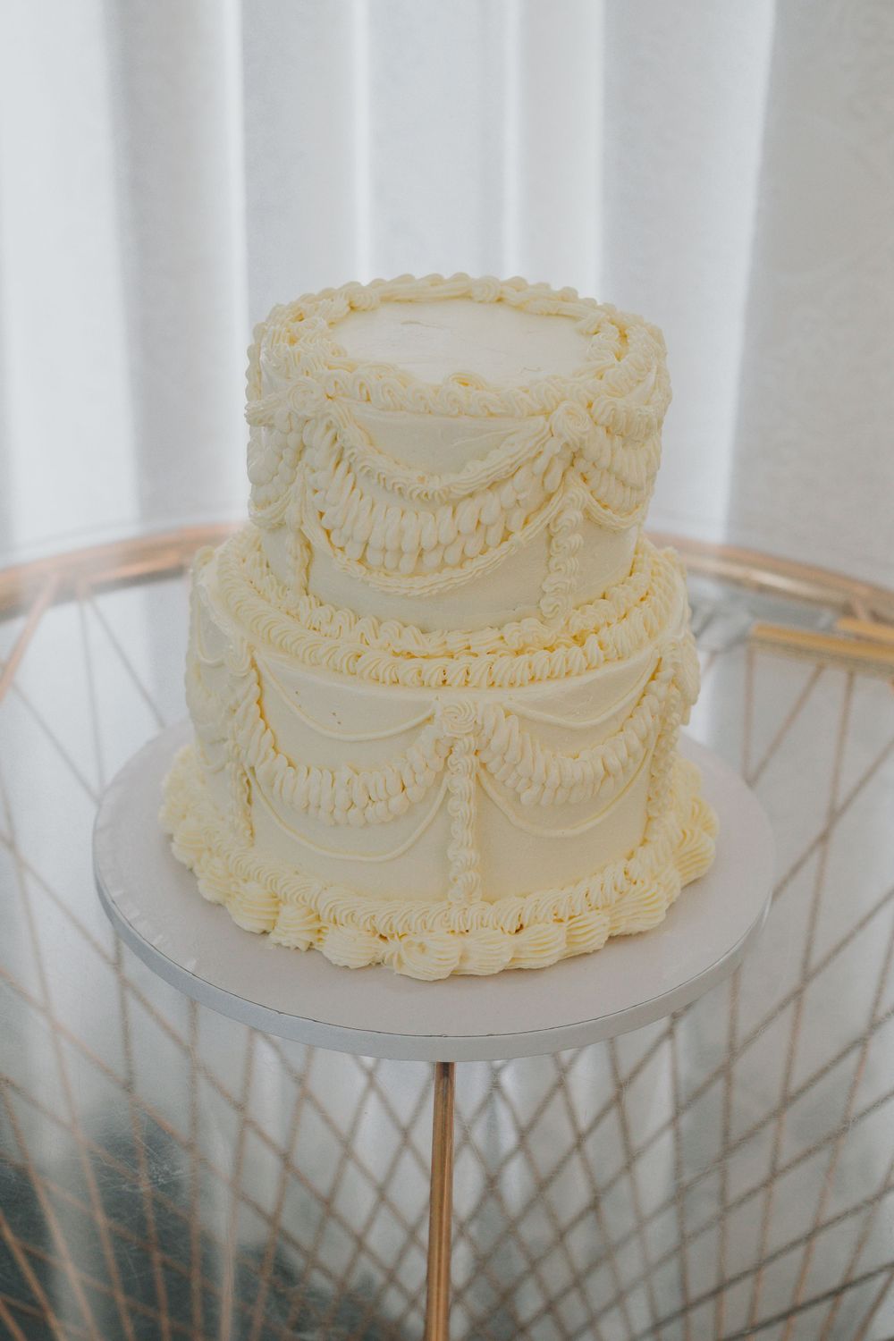 Two-tier cream colored wedding cake with delicate piped swag details and pearl borders.