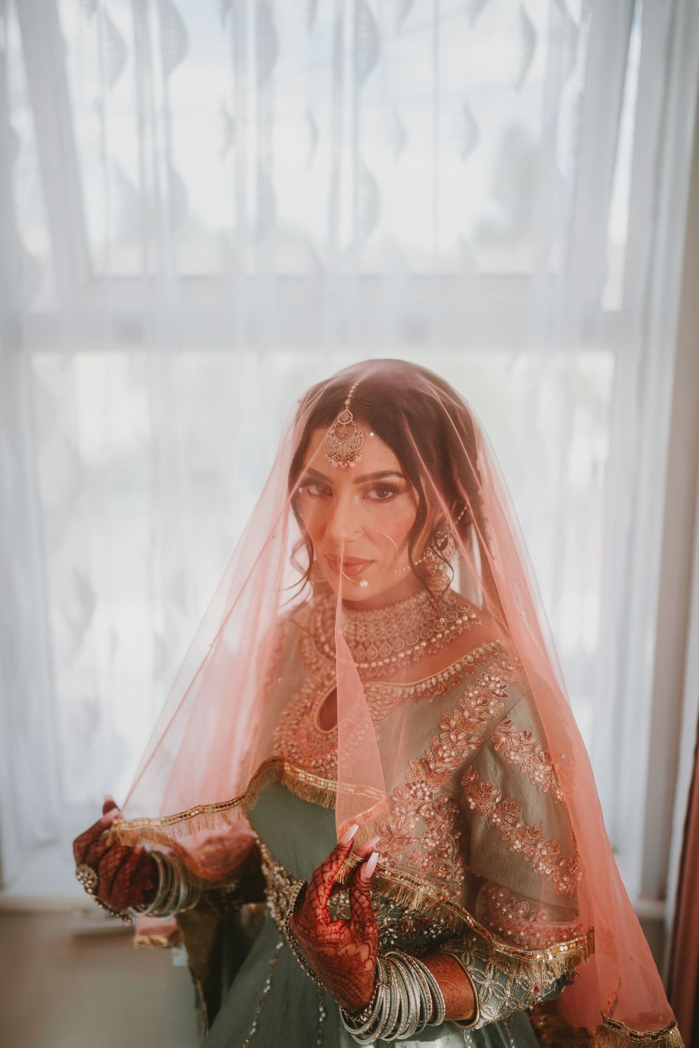 Traditional South Asian bridal attire featuring intricate embroidery and delicate veil in warm tones.