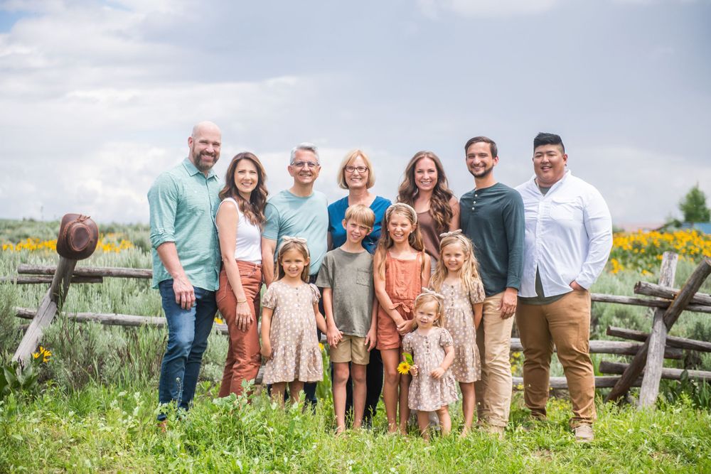 Group gathered by rustic wooden fence in sunny meadow with wildflowers and natural scenery.