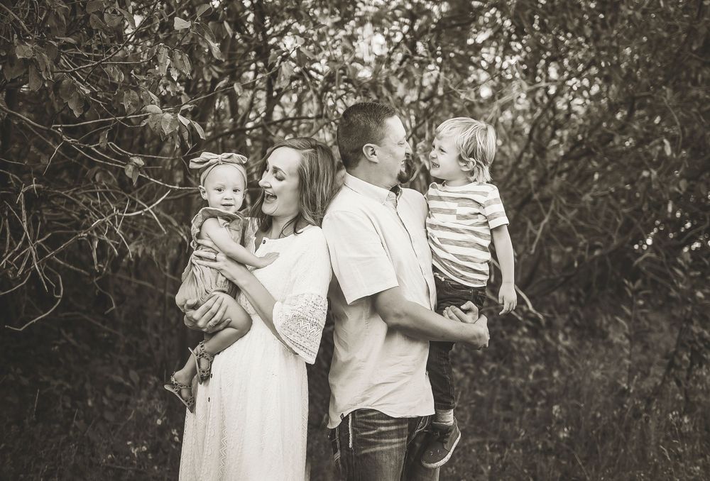 A joyful family of four captured in black and white photography outdoors among natural foliage.
