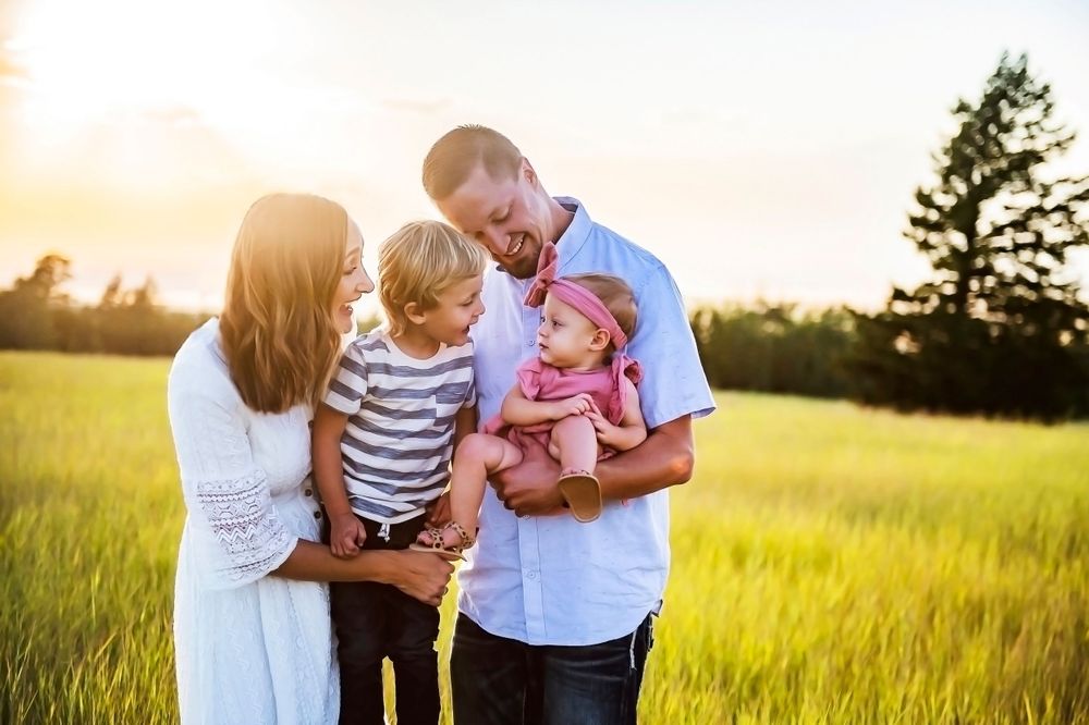 A loving family shares a tender moment together in a sunlit field of golden grass at sunset.