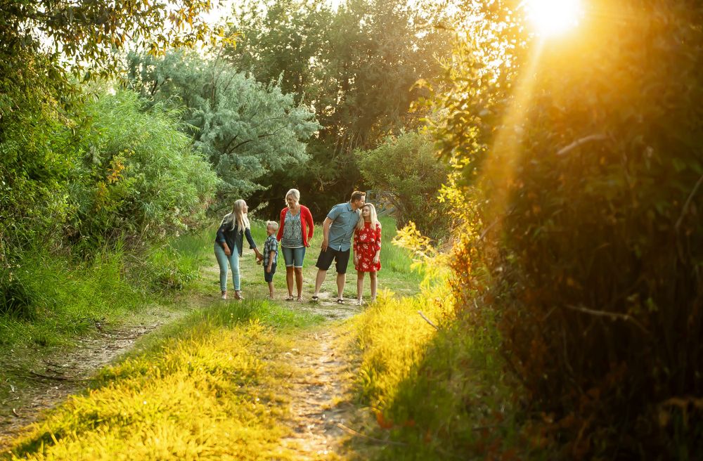 People hiking on a dirt trail through lush greenery at golden sunset with sun flare illuminating the path.