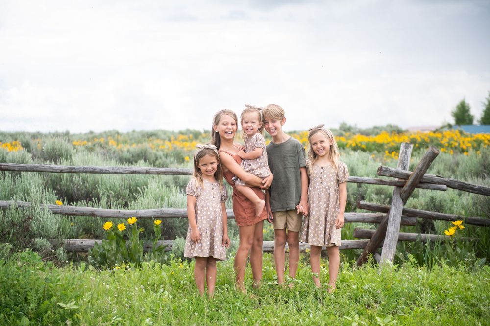 Children standing together by rustic wooden fence in field of yellow wildflowers.