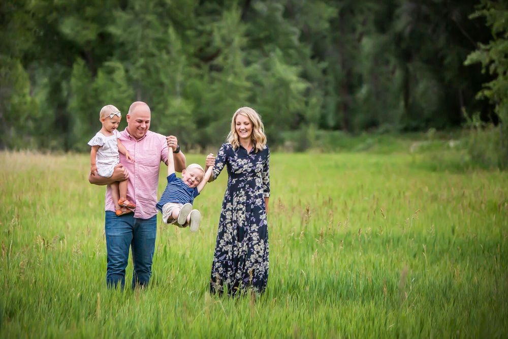 A family holds hands while walking together through a green summer meadow with trees in the background.