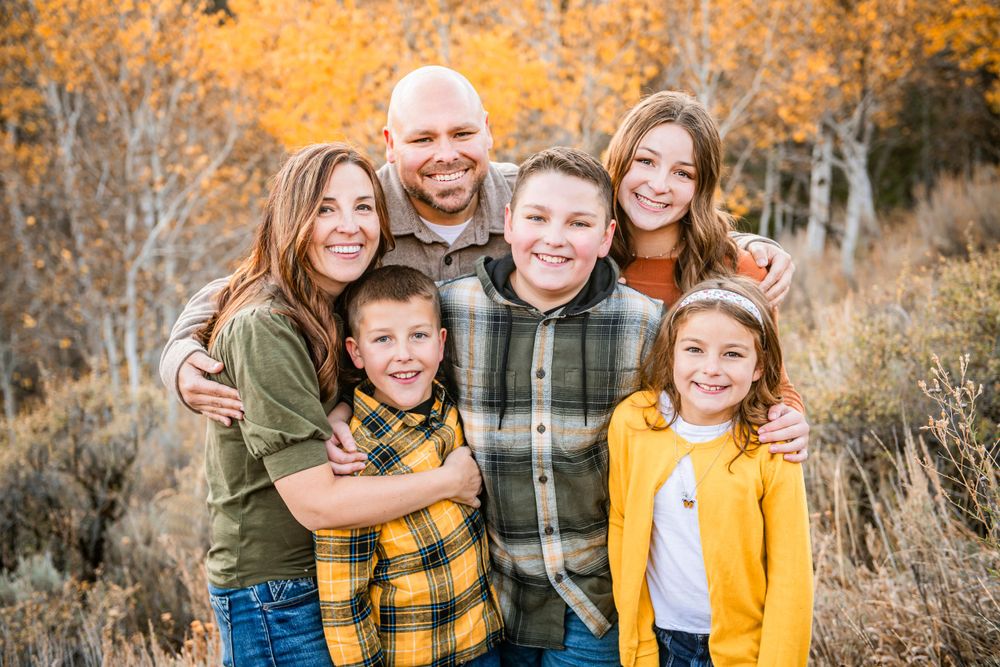 A family poses together in nature during autumn with golden foliage and brush in the background.