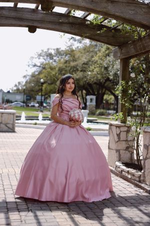 Sweet sixteen showing off her beautiful pink gown, holding her bouquet standing under the garden bridge.