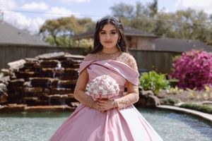 Sweet sixteen outdoor session/portrait model is in front a water cascade while model is holding her pink bouquet.