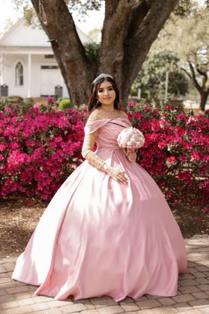 sweet sixteen outdoor portrait of model standing in front of beautiful deep pink flowers