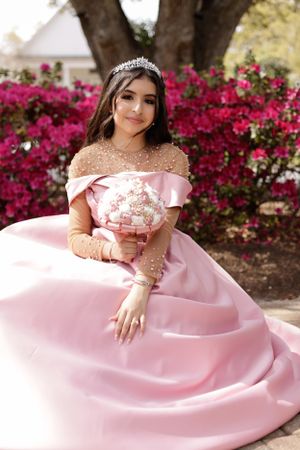 Sweet sixteen outdoor session/portrait of model sitting on the floor to poof her dress and showing off the flowers in the background.