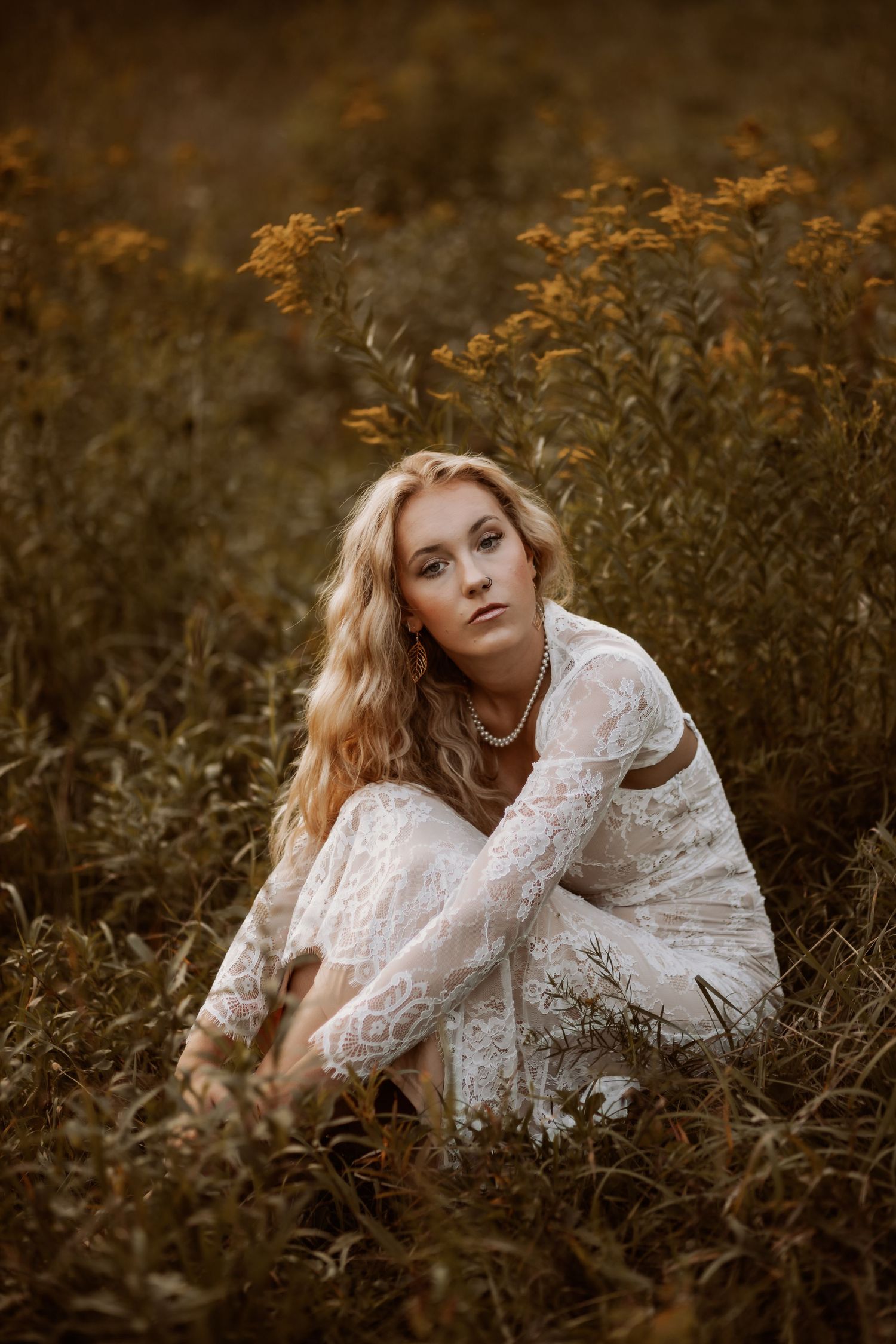 A woman in a lace dress poses in a golden autumn field during sunset.