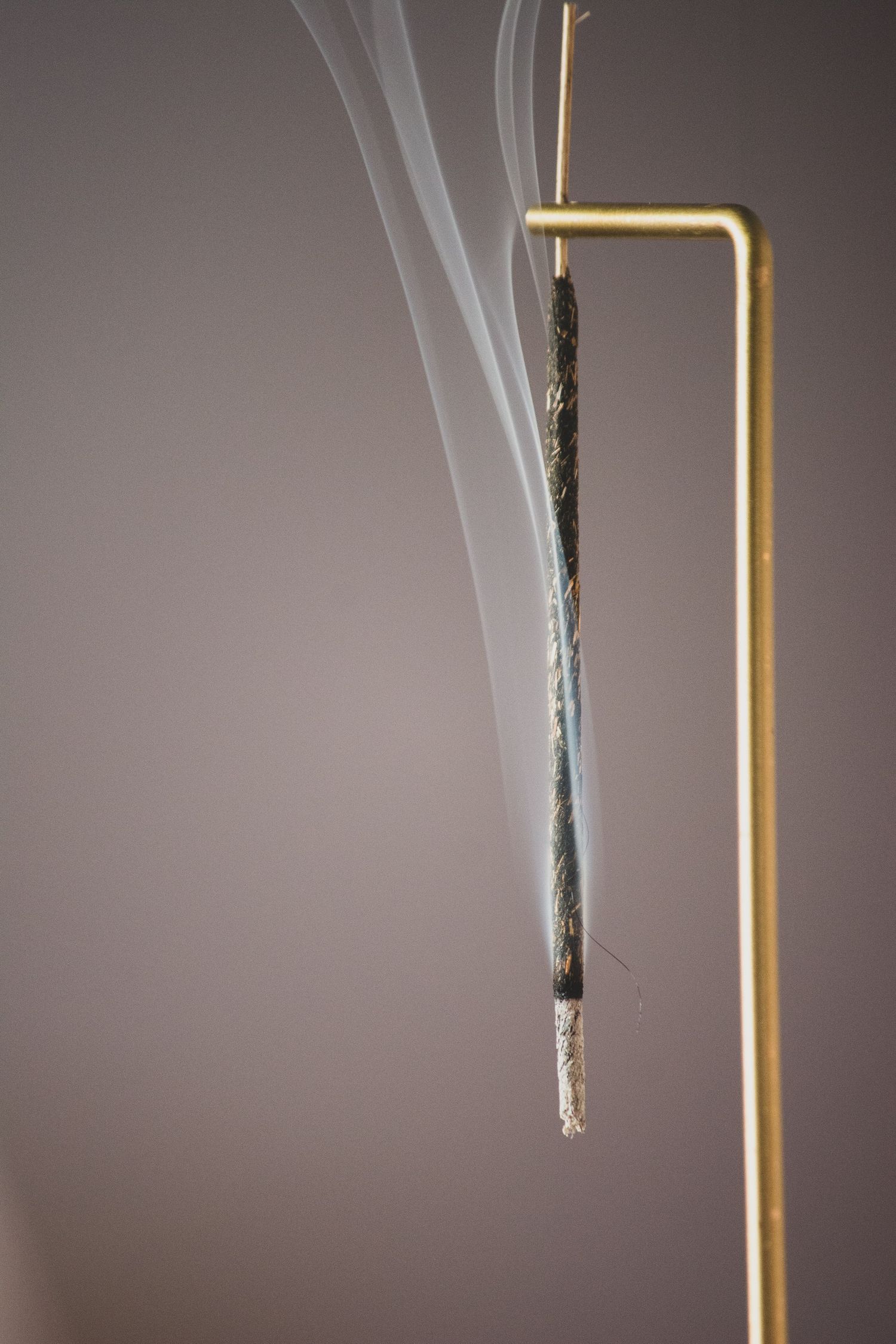 a product photo of smoke leaving an incense stick on a gold holder against a brown background