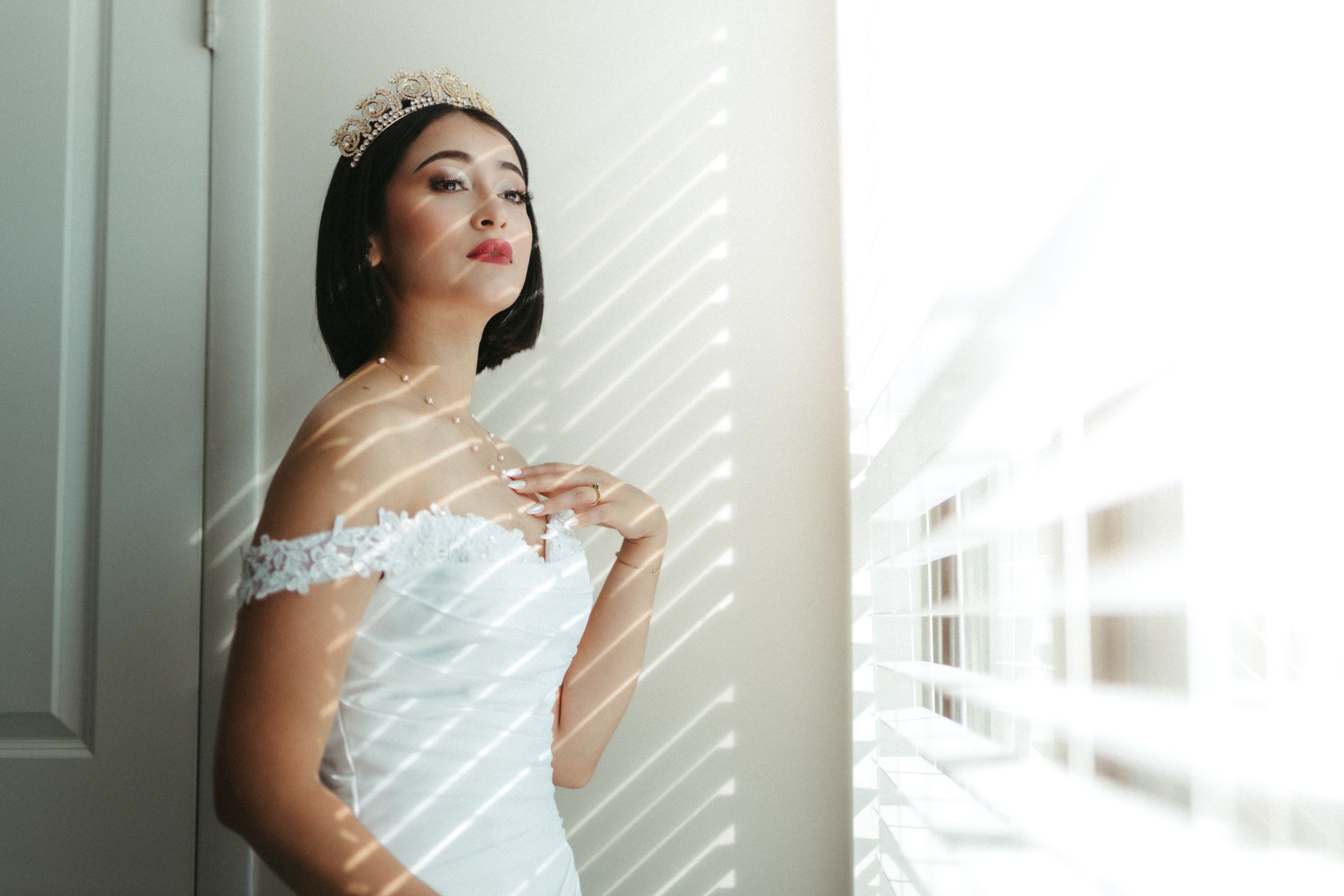 Serene portrait by a window showing a delicate off-shoulder white lace dress in soft natural lighting.