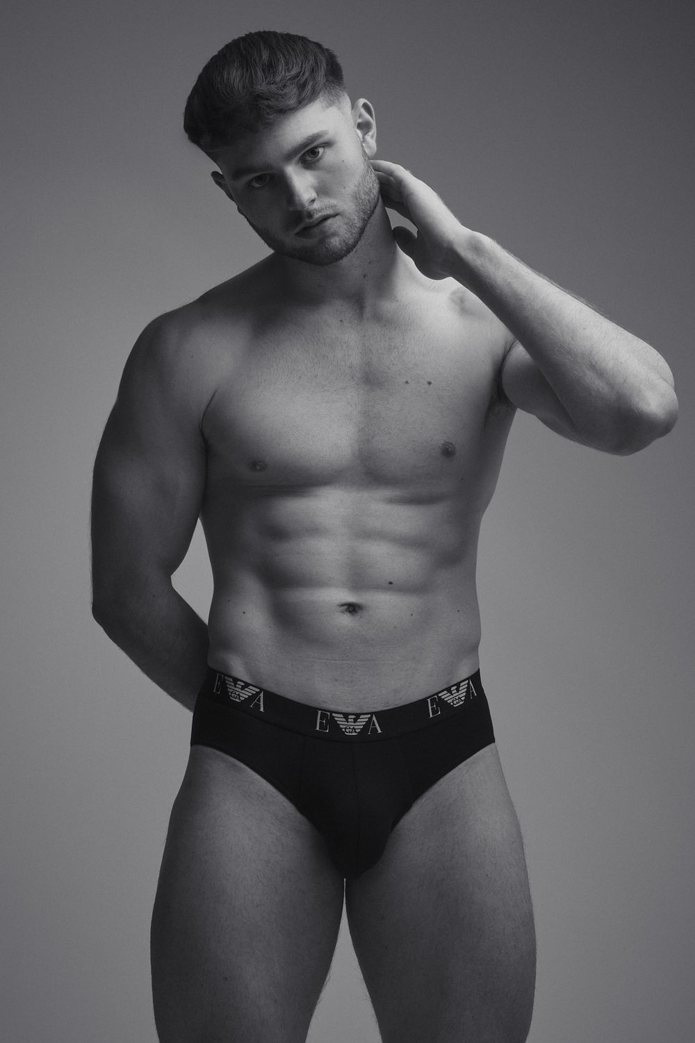 Black-and-white shot of a muscular male model in Emporio Armani briefs, posed confidently against a neutral backdrop